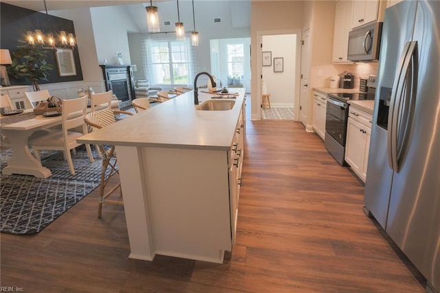 kitchen with appliances with stainless steel finishes, white cabinetry, an island with sink, decorative light fixtures, and sink