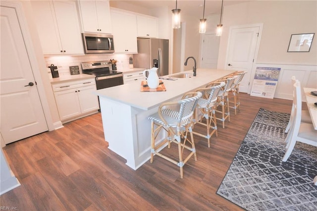 kitchen featuring hanging light fixtures, a kitchen island with sink, stainless steel appliances, and white cabinetry