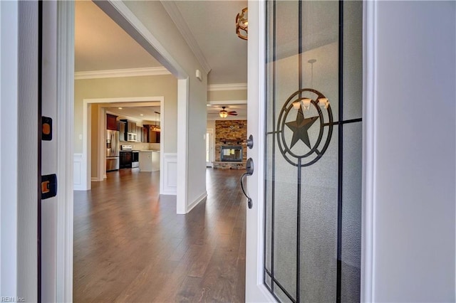 foyer entrance featuring crown molding, a stone fireplace, dark wood-type flooring, and ceiling fan