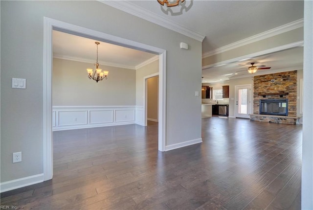 unfurnished living room with ceiling fan with notable chandelier, a stone fireplace, crown molding, and dark wood-type flooring