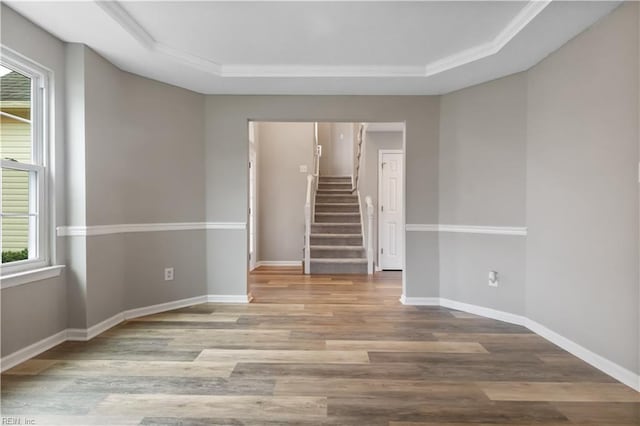 unfurnished room with wood-type flooring, a raised ceiling, and crown molding