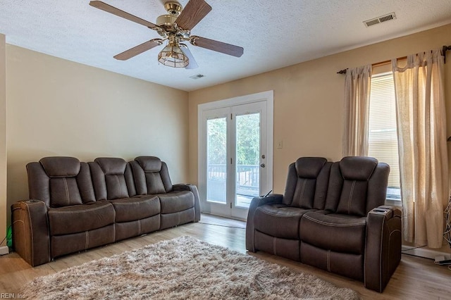 living room with ceiling fan, light wood-type flooring, and a textured ceiling