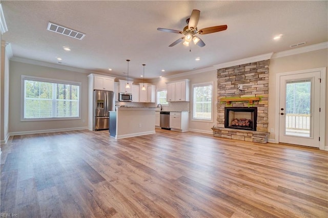 unfurnished living room with a healthy amount of sunlight, a stone fireplace, ceiling fan, and light hardwood / wood-style flooring