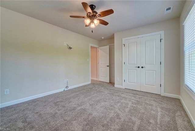 unfurnished bedroom featuring a closet, multiple windows, light colored carpet, and ceiling fan