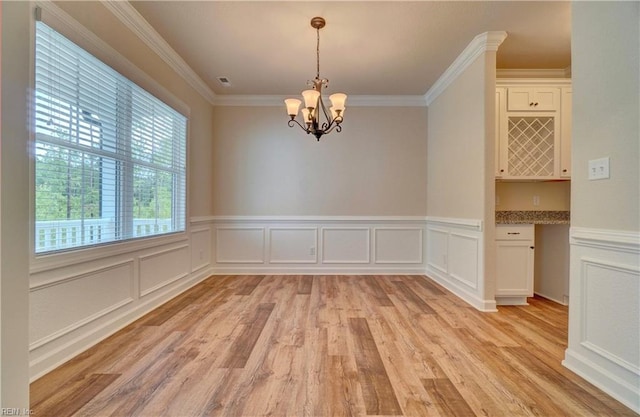 unfurnished dining area with light hardwood / wood-style flooring, an inviting chandelier, and crown molding