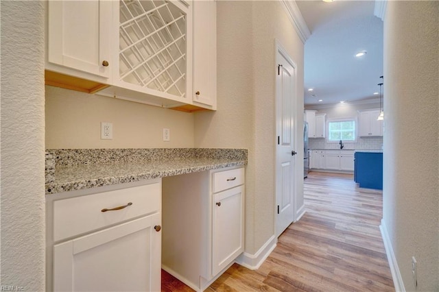 kitchen featuring light wood-type flooring, stainless steel fridge, white cabinetry, light stone countertops, and crown molding