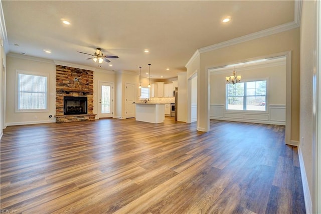 unfurnished living room with ceiling fan with notable chandelier, dark wood-type flooring, a fireplace, and crown molding