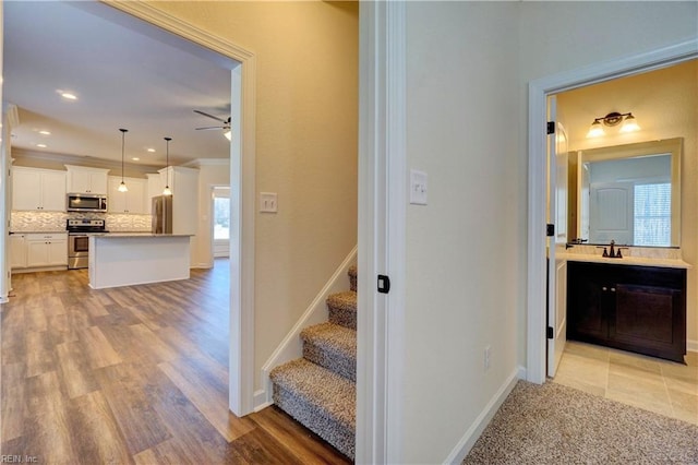 staircase featuring crown molding, sink, ceiling fan, and hardwood / wood-style flooring