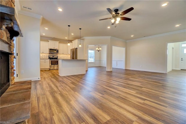 unfurnished living room with ceiling fan with notable chandelier, light wood-type flooring, crown molding, and a stone fireplace