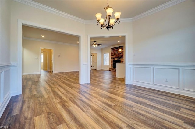 empty room with ceiling fan with notable chandelier, a fireplace, ornamental molding, and hardwood / wood-style floors