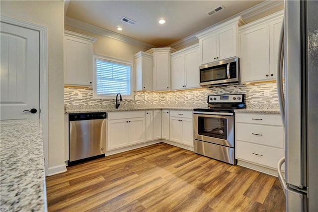 kitchen with light stone counters, white cabinets, ornamental molding, appliances with stainless steel finishes, and light hardwood / wood-style floors