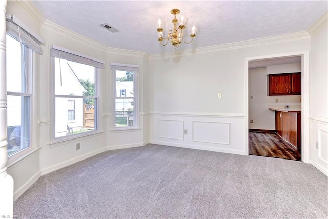 carpeted spare room featuring a healthy amount of sunlight, ornamental molding, and a chandelier