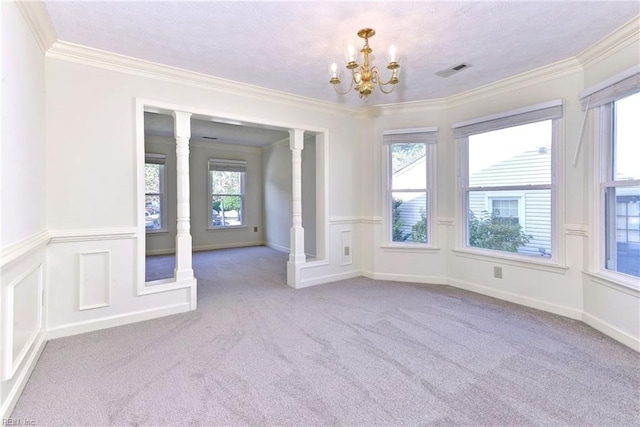 carpeted empty room featuring decorative columns, ornamental molding, and a notable chandelier