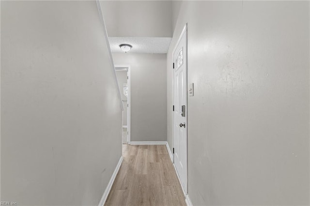 corridor with a textured ceiling and light hardwood / wood-style floors