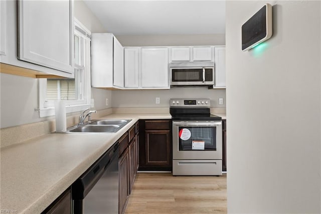 kitchen with appliances with stainless steel finishes, white cabinets, light wood-type flooring, dark brown cabinetry, and sink