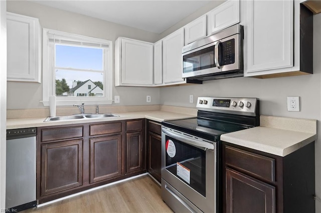 kitchen featuring appliances with stainless steel finishes, white cabinetry, sink, and light hardwood / wood-style flooring