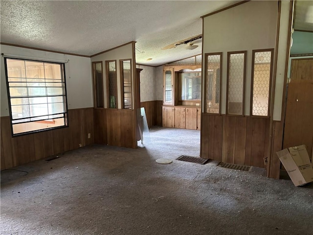 empty room with light carpet, a textured ceiling, wood walls, and vaulted ceiling