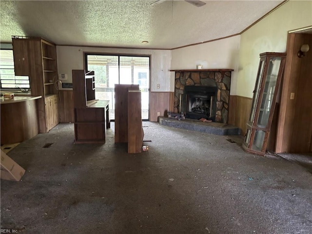 unfurnished living room with dark carpet, a textured ceiling, wood walls, a stone fireplace, and ornamental molding