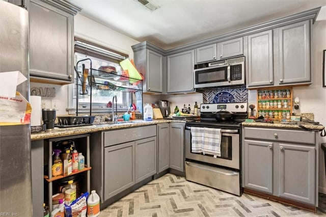 kitchen featuring dark stone counters, gray cabinetry, sink, and stainless steel appliances