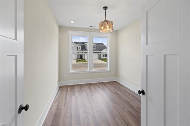 empty room featuring wood-type flooring and an inviting chandelier