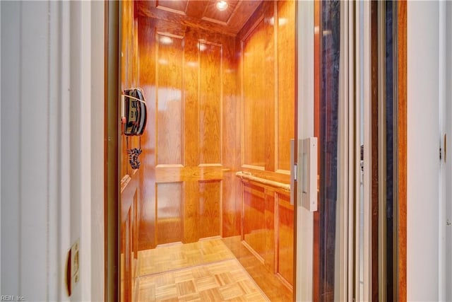 corridor featuring elevator, wood walls, and parquet flooring