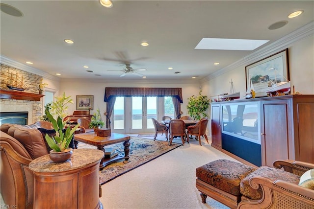 living room featuring ceiling fan, a skylight, ornamental molding, a stone fireplace, and light carpet