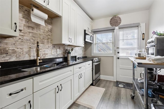 kitchen with light hardwood / wood-style flooring, appliances with stainless steel finishes, dark stone counters, and white cabinetry