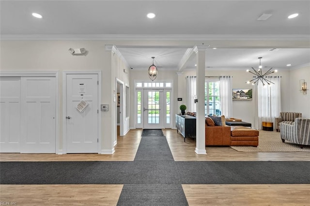 entryway with crown molding, decorative columns, an inviting chandelier, and light hardwood / wood-style flooring