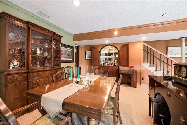 carpeted dining space with a textured ceiling, crown molding, and indoor bar