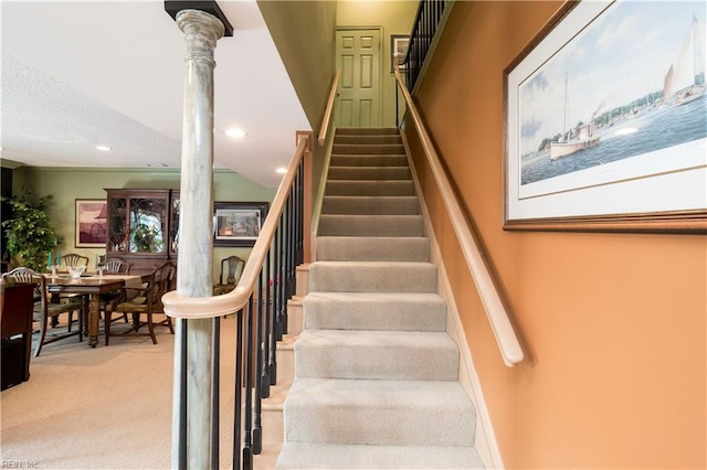 stairway with carpet floors, decorative columns, and a textured ceiling