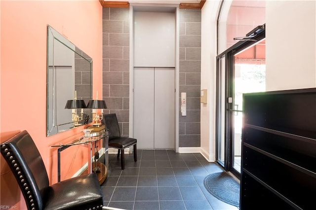 interior space with dark tile patterned flooring, tile walls, and elevator