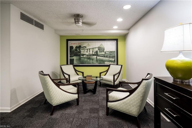 living area featuring a textured ceiling, carpet flooring, and ceiling fan