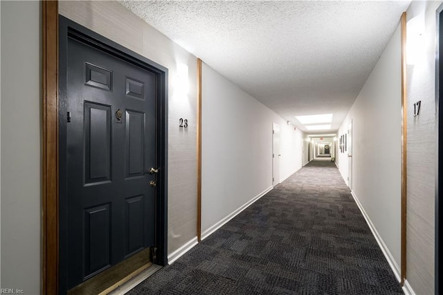 hallway with dark colored carpet and a textured ceiling