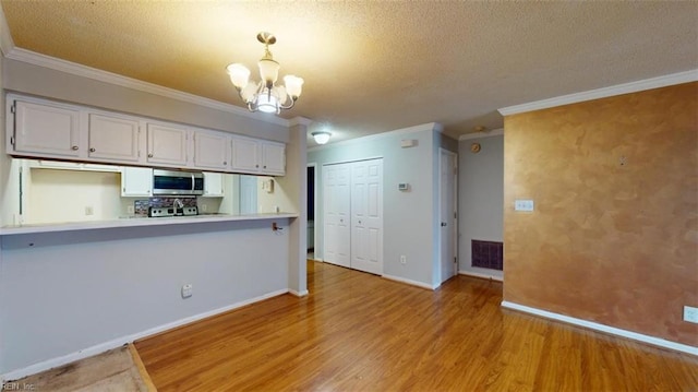 kitchen with hanging light fixtures, light hardwood / wood-style floors, white cabinets, crown molding, and an inviting chandelier