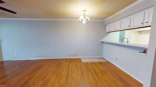 empty room featuring a textured ceiling, sink, ceiling fan with notable chandelier, light hardwood / wood-style flooring, and ornamental molding