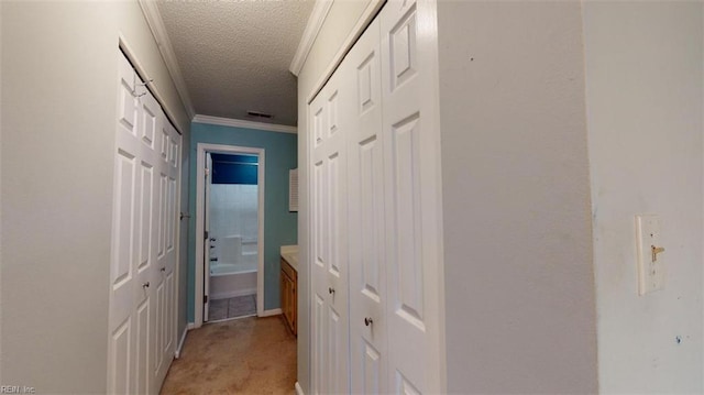 hallway with a textured ceiling, ornamental molding, and light colored carpet