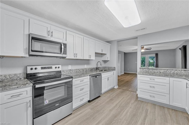 kitchen featuring a textured ceiling, appliances with stainless steel finishes, light wood-type flooring, and white cabinetry