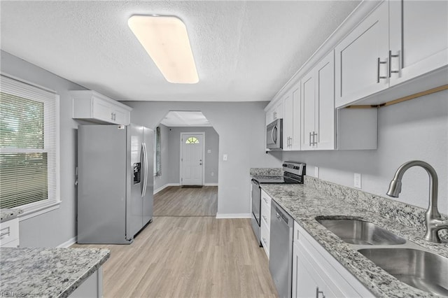 kitchen featuring light wood-type flooring, light stone counters, sink, white cabinetry, and appliances with stainless steel finishes