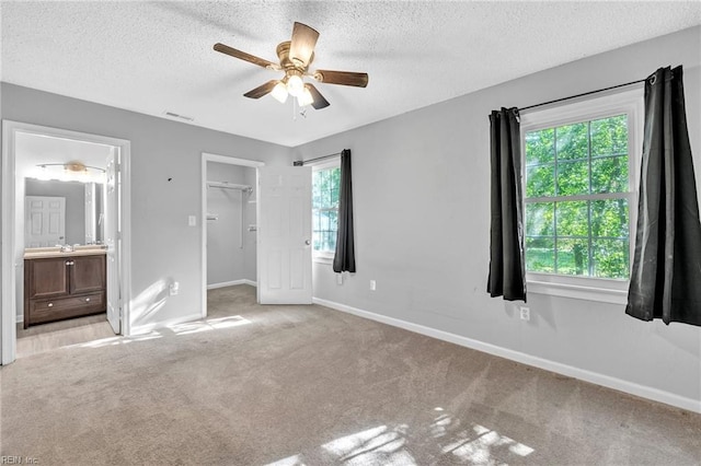 unfurnished bedroom featuring light carpet, ensuite bathroom, multiple windows, and ceiling fan