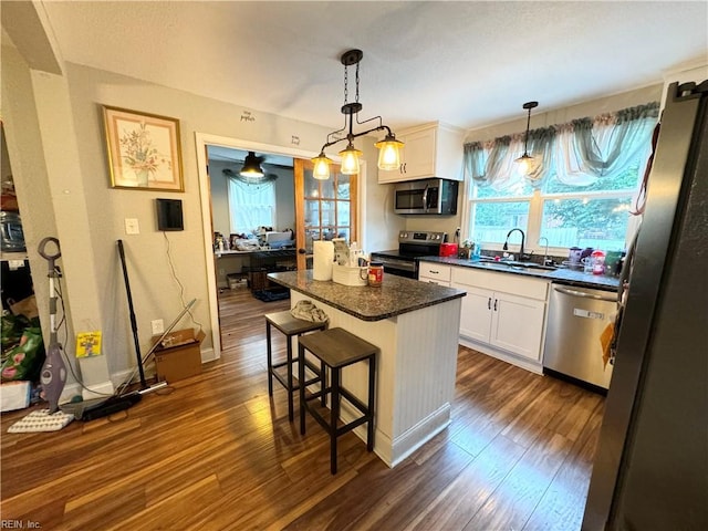 kitchen featuring appliances with stainless steel finishes, white cabinetry, a kitchen island, dark hardwood / wood-style flooring, and a kitchen bar