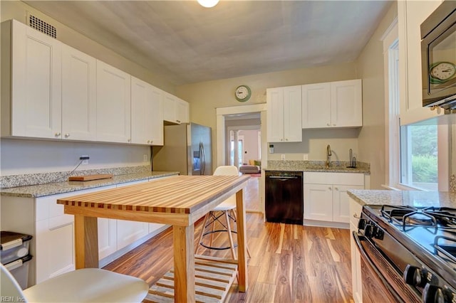 kitchen with light wood-type flooring, black appliances, white cabinetry, and light stone counters