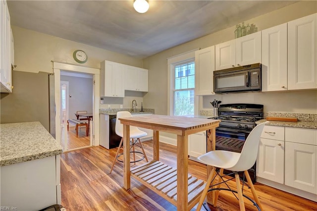 kitchen featuring light wood-type flooring, black appliances, and white cabinetry