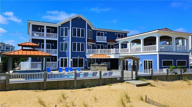 rear view of property with a balcony, a pool, and a gazebo