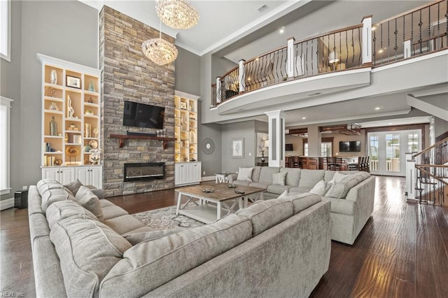 living room featuring dark hardwood / wood-style flooring, a notable chandelier, a fireplace, a towering ceiling, and crown molding