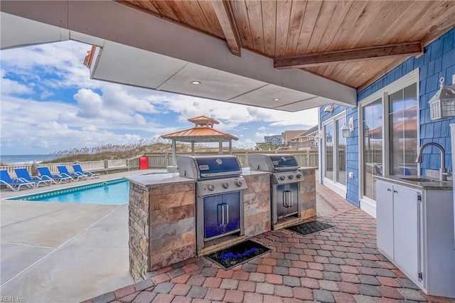 view of patio featuring a community pool, a grill, an outdoor kitchen, and sink