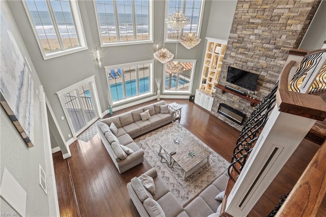 living room with a towering ceiling, a chandelier, dark wood-type flooring, and a stone fireplace