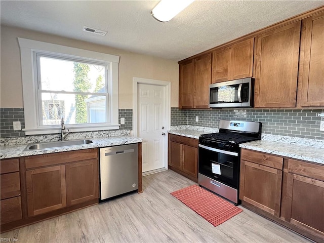 kitchen with appliances with stainless steel finishes, light hardwood / wood-style floors, light stone countertops, a textured ceiling, and sink