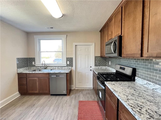 kitchen featuring appliances with stainless steel finishes, a textured ceiling, light wood-type flooring, and sink