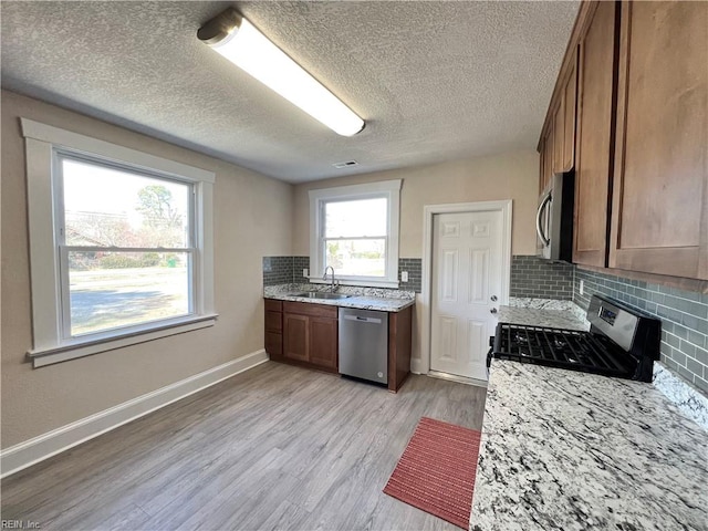 kitchen featuring tasteful backsplash, stainless steel appliances, light wood-type flooring, a textured ceiling, and sink