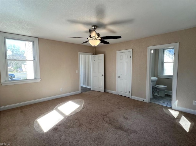 unfurnished bedroom with ceiling fan, carpet, ensuite bathroom, and multiple windows